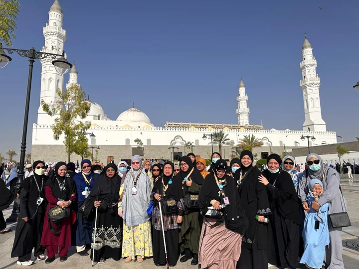 Pilgrims pose together in front of a white-domed mosque.