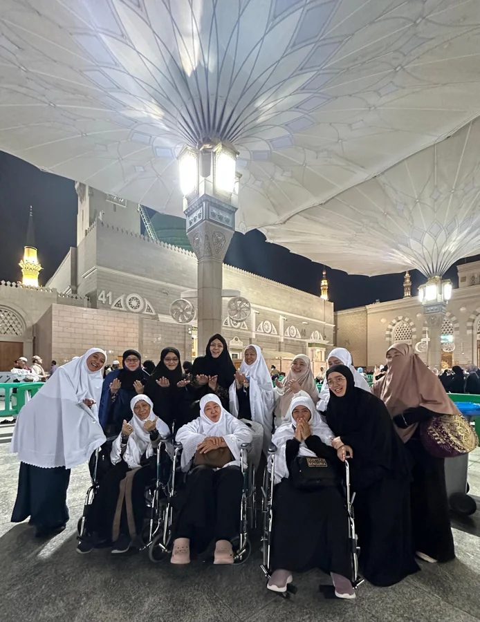 Pilgrims gather under large canopies in the mosque courtyard at night.