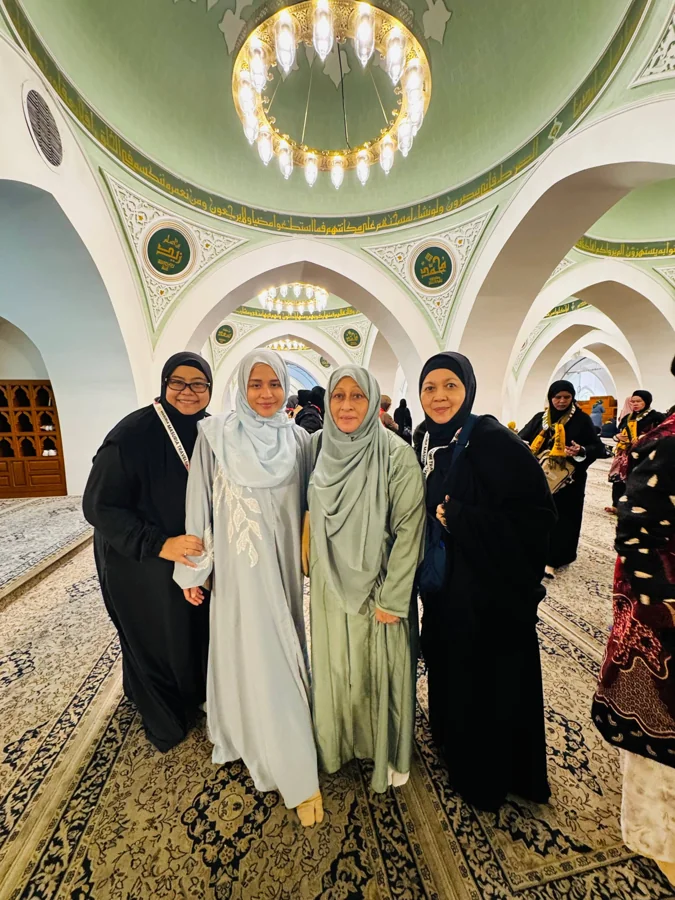 Four pilgrims pose beneath an ornate mosque ceiling and arches.